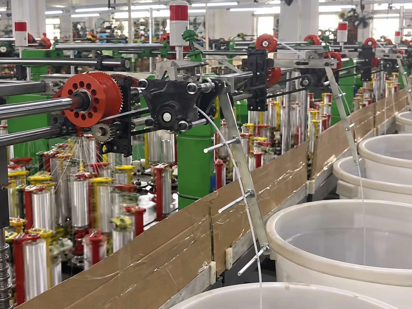 Cable braiding machines with yarn spools and collection bins on a production line