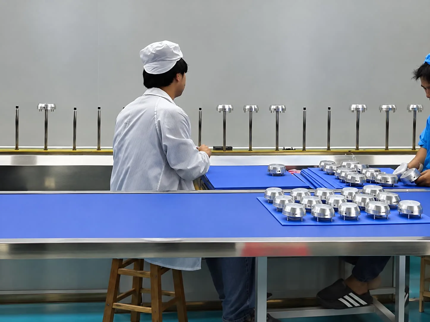 Workers preparing components at the loading station of a spray coating production line.
